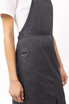 A black bib apron with a pocket and a metal ring detail, worn by a person against a neutral background.