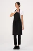 A black Lockharte Bib Apron worn by a model, featuring ties at the waist and a branding logo.