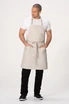 A beige bib apron worn by a model, featuring two front pockets and adjustable straps.