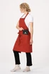 A red bib apron worn by a person, featuring a pocket, styled with casual black pants and sneakers.
