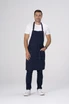 A navy blue bib apron with adjustable straps, worn by a smiling man in casual clothing and white shoes.