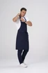 A model wearing a navy blue Lockharte Bib Apron, paired with a white t-shirt and dark jeans, featuring a logo.