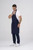 A man in a navy blue apron adjusts it while wearing a white t-shirt and dark jeans. The apron has a branding logo.