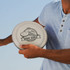 A person holds a large grey disc with a disc golf design and logo, wearing a light blue shirt.