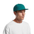 A teal cap with a flat brim and a branded logo on the front, worn by a model in a white shirt.
