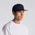 A navy trucker cap with a flat brim, featuring a logo, worn by a model in a white T-shirt.