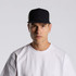 A black and white trucker cap with a logo, worn by a person in a white t-shirt.