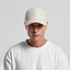 A light beige nylon cap displayed on a model wearing a white sweatshirt. The cap features a logo.