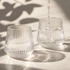 A drink bottle featuring a ribbed design, made of clear glass, with water being poured into two glasses.