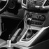 A dual car charger in white, plugged into a vehicle's centre console, next to the gear shift and dashboard controls.