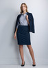 A woman in a navy 3/4 sleeve shirt and matching skirt stands confidently, wearing a blazer and high heels.