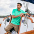 A man wearing a mint green polo shirt sits on a boat, surrounded by ropes and wooden elements.