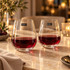 A set of two clear stemless wine glasses filled with red wine, placed on a marble table with soft lighting.