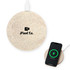 A round, sandy-coloured wireless charger with a logo, beside a smartphone displaying a charging icon.