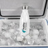 A drink bottle in white with a silver cap, nestled among ice cubes in a cooler, featuring a logo.