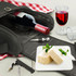 A black picnic bag containing a wine bottle, wine glass, cheese, and a corkscrew set on a table.