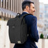 A black Osprey Arcane Flap Backpack is worn on the back of a man in a suit, standing outdoors.