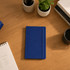A blue journal book lies on a wooden desk next to a cup, potted plant, and stationery supplies.