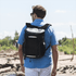 A black backpack cooler with a sleek design, worn by a man in a casual blue shirt against a natural backdrop.