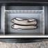 A silver multi-tool featuring several tools, placed inside a grey storage compartment. The tool has a branded logo.