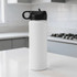 A drink bottle in white with a black lid, featuring a handle, set against a kitchen backdrop.