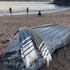 A grey and blue striped towel draped over a weathered boat on a sandy beach, with people in the background.