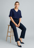 A woman sits on a stool wearing navy slacks and a navy top, paired with matching heels. The outfit has a modern design. A woman sits on a stool wearing navy slacks and a navy top, paired with matching heels. The outfit has a modern design.