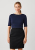A navy short sleeve T-shirt paired with a black fitted skirt on a model. The shirt features a round neckline and has branding.