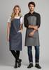 Two models wearing Urban Bib Aprons in navy blue and grey, featuring pockets and adjustable straps. Each apron has a logo.