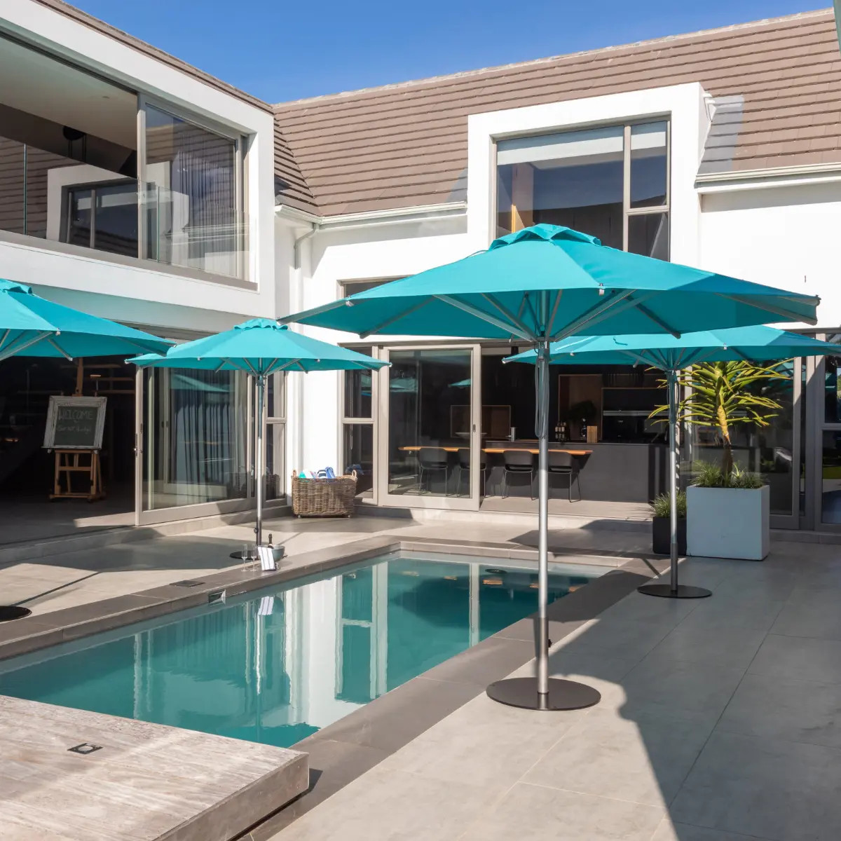Woodline Pacific Umbrellas with aluminum poles and teal canopies around a swimming pool