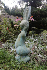 Silly Bunny statue in copper rust finish among the garden