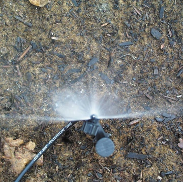 DripWorks 180-Degree Micro-Jet Sprayer emitting a half-circle water pattern over soil