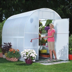 Person watering plants inside a Solexx Oasis Greenhouse with a hose.