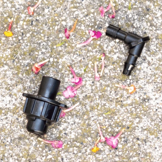 DripWorks Elbow Mister disassembled on pebbles with flower petals