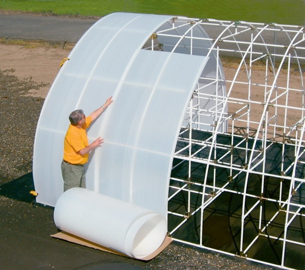 Person installing Solexx greenhouse covering roll onto a metal hoop structure.