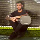 Pickleball pro player DJ Young sitting against a chain link fence while holding the CRBN-1X Power Series Carbon Fiber Paddle