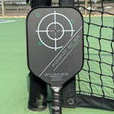 Engage Pursuit MAXX EX 6.0 Friction Carbon Pickleball Paddle leaning against net on court.