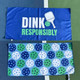 View of both sides of the Born to Rally Dink Responsibly Double-Sided Microfiber Towel in the color Blue displayed on pickleball court.