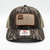 Professional product studio photograph displaying a Mossy Oak Bottomland Winter Timber Outdoors mesh-back trucker cap centered against a bright, clean white background. The hat is built on a classic Richardson 112 frame featuring a structured brown cotton front panel, white contrast brim stitching, and tan breathable mesh rear paneling. Prominently centered on the crown is a rectangular brown border embroidered patch featuring a beige field styled like the American flag, detailed with "Winter Timber" text and rows of duck, turkey, and deer wildlife silhouettes. The brim retains the authentic black and silver oval "Richardson 112 The Original" brand sticker in the lower center.