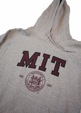 Classic sport grey MIT hooded sweatshirt featuring bold varsity lettering and the official MIT Crest. Soft, durable with a front pocket and drawstring hood. Timeless collegiate style.