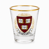 Clear Harvard crest shot glass with maroon and gold design and gold-tone rim on white background