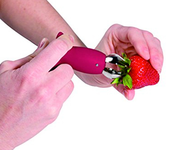 Hands holding the strawberry huller with its claw open over the stem of a strawberry.