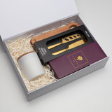 A gift box containing a white candle, wooden spoon, and a black knife set with gold accents, surrounded by crinkle paper.