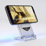A clear acrylic wireless charging stand holding a smartphone, featuring a logo at its base. The stand has a sleek design.
