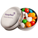 A branded metal tin filled with colourful chewy fruit candies, featuring a logo on the top.