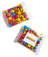 A branded bag contains colourful chocolate-coated sweets, including pink, purple, blue, yellow, orange, and brown candies.