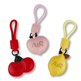 Three bag charms in red, pink, and yellow, featuring apple and lemon shapes with one charm having a logo.