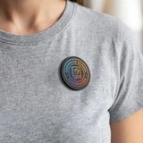 A person wearing a grey t-shirt with a round, multicoloured badge featuring a logo, attached to the chest area.
