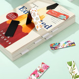 A collection of large bookmarks featuring various vibrant floral and festive designs, placed on a book.