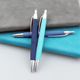 Three plastic pens in navy blue and light blue resting on textured grey and turquoise surfaces, featuring metallic accents.